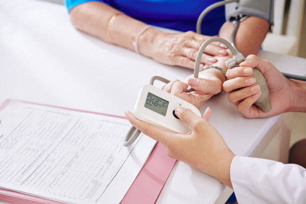 Sairaanhoitaja tarkistaa senioripotilaan verenpaineen elektronisella tonometrillä vuosittaisen tarkastuksen aikana - Valokuva, kuva