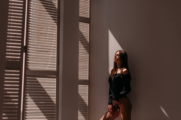 Young beautiful girl model, tall, in a black body, in a large bright room, bright sunlight from the window falls on her - 写真・画像