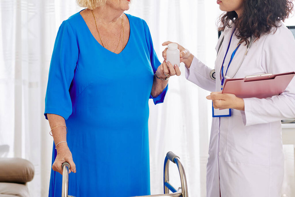 Arzt mit Klemmbrett gibt älteren Patienten Tabletten oder Nahrungsergänzungsmittel - Foto, Bild