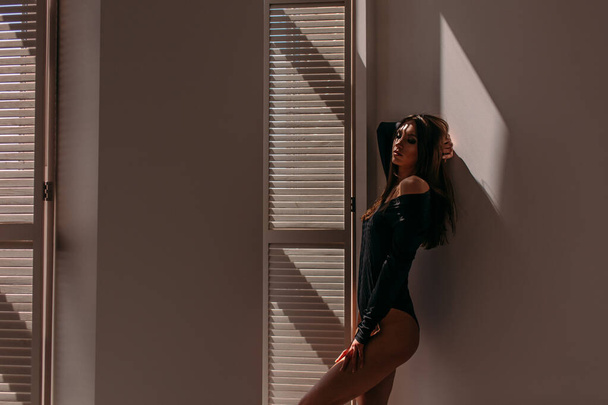 Young beautiful girl model, tall, in a black body, in a large bright room, bright sunlight from the window falls on her - Foto, Imagem
