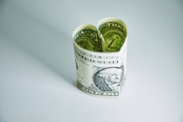 Сердце сложено из одной долларовой купюры на сером фоне с копировальным пространством. Концепция имиджа денежной любви
 - Фото, изображение