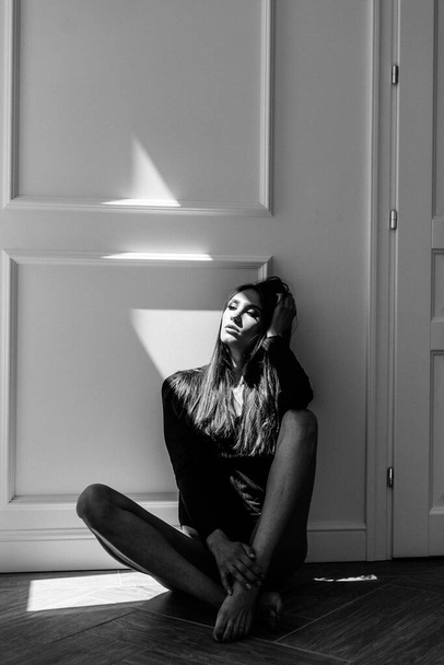 Young beautiful girl model, tall, in a black body, in a large bright room, bright sunlight from the window falls on her - Foto, imagen