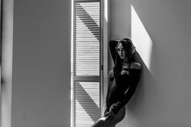 Fiatal gyönyörű lány modell, magas, egy fekete test, egy nagy fényes szobában, fényes napfény az ablakból esik rá - Fotó, kép