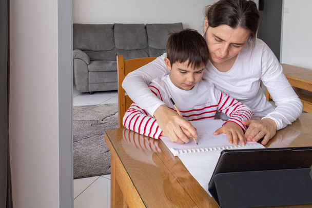 Moeder helpt haar zoon om huiswerk te maken, thuisonderwijs, kleine jongen leren thuis op afstand - Foto, afbeelding