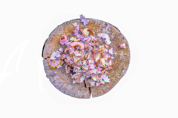 Wooden pencil shavings and colorful crumbs of graphite from sharpener on a tree stump on white background. Top view. - Photo, Image