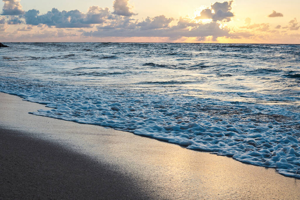 Pôr do sol no mar rochoso. Água azul-turquesa no oceano à noite.Céu amarelo com pequenas nuvens e ondas azuis na praia de areia à beira-mar.Paisagem balneária.Close-up picture of ocean waves
 - Foto, Imagem