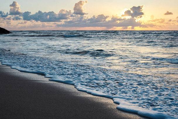 Pôr do sol no mar rochoso. Água azul-turquesa no oceano à noite.Céu amarelo com pequenas nuvens e ondas azuis na praia de areia à beira-mar.Paisagem balneária.Close-up picture of ocean waves
 - Foto, Imagem