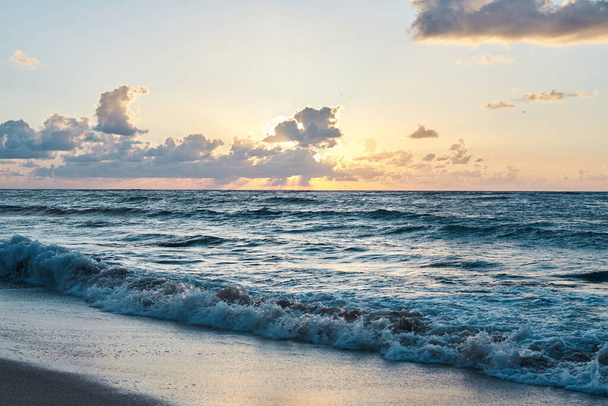 Sunset at the rocky sea. Turquoise water in the ocean in the evening.Yellow sky with small clouds and blue waves at sandy beach at the seaside.Paradise resort landscape.Close-up picture of ocean waves - Photo, image