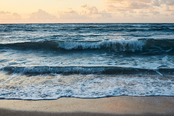 Zachód słońca nad skalistym morzem. Turkusowa woda w oceanie wieczorem Żółte niebo z małymi chmurami i niebieskimi falami na piaszczystej plaży nad morzem Raj landscape.Close-up obraz fal oceanicznych - Zdjęcie, obraz