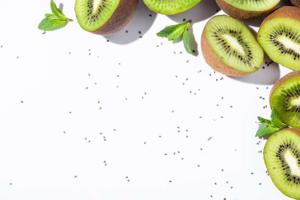 top view of organic kiwi fruit halves near peppermint and black seeds on white  - Photo, Image