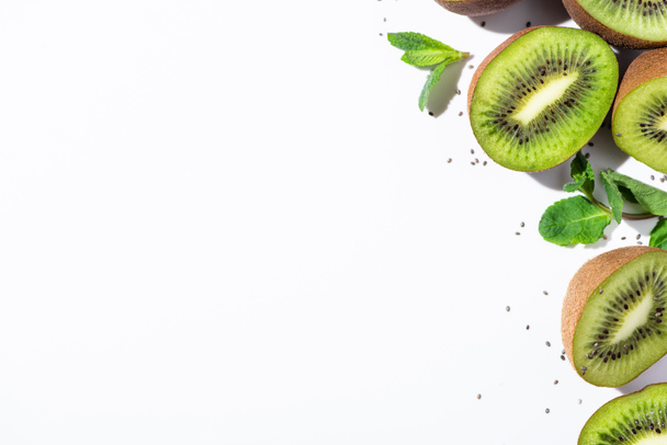 top view of tasty kiwi fruit halves near green peppermint and black seeds on white  - Photo, Image
