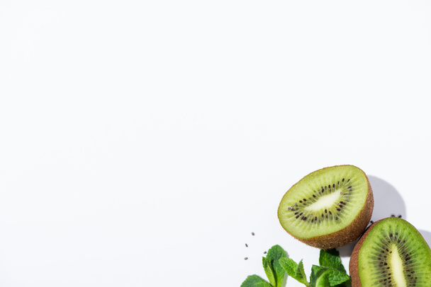 bovenaanzicht van smakelijke kiwi 's nabij verse pepermunt en zwarte zaden op wit  - Foto, afbeelding