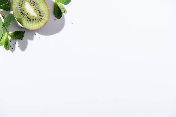 top view of green peppermint near fresh kiwi fruit and black seeds on white - Zdjęcie, obraz