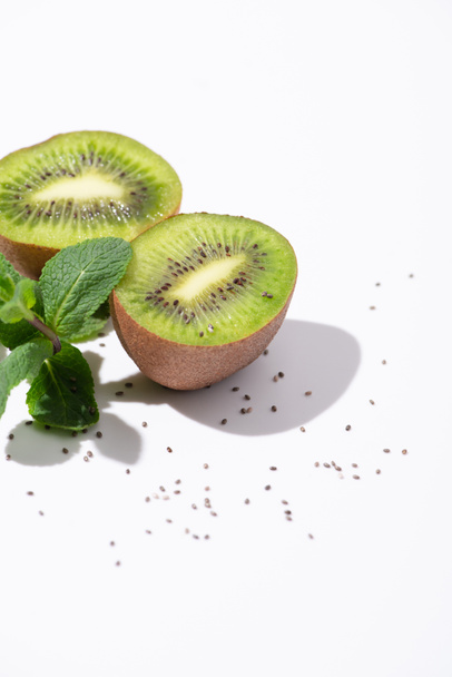 sabrosas frutas kiwi cerca de menta fresca y semillas negras sobre blanco
  - Foto, Imagen