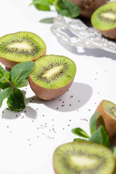 selective focus of green kiwi fruits near peppermint and black seeds on white  - Photo, Image