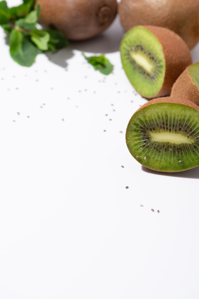 selective focus of fresh kiwi fruits near green peppermint and black seeds on white  - Photo, Image