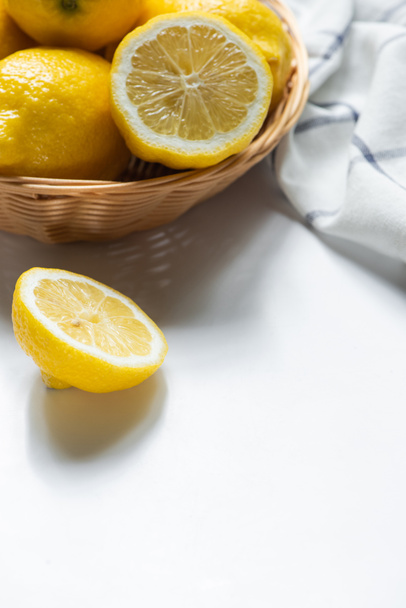 close up view of basket of fresh lemons and napkin on white background - Foto, afbeelding