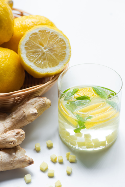 close up view of fresh lemonade with mint in glass near basket of lemons and ginger root on white background - Fotografie, Obrázek
