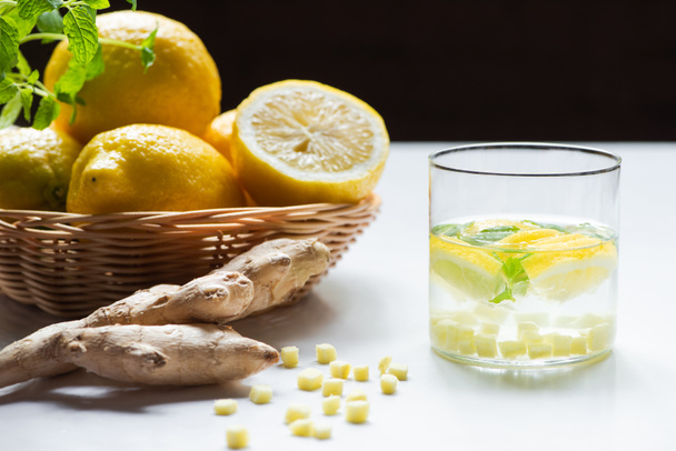 fresh lemonade with mint in glass near basket of lemons and ginger root on white background isolated on black - 写真・画像