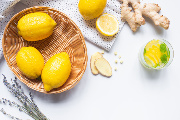 top view of fresh lemonade in glass near basket of lemons, lavender and ginger root on white background with napkin - Foto, Bild