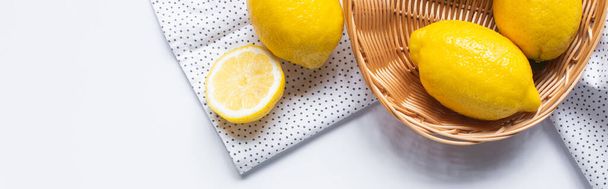 bovenaanzicht van rijpe citroenen in rieten mandje op witte achtergrond met gestippelde servet, horizontaal beeld - Foto, afbeelding