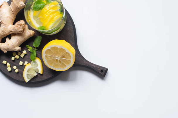 top view of fresh lemonade in glass near lemons and ginger root on black wooden board on white background - Foto, imagen