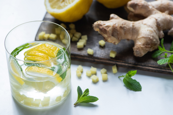 selective focus of fresh ginger lemonade in glass with lemon and mint on wooden board on white background - Foto, Imagem