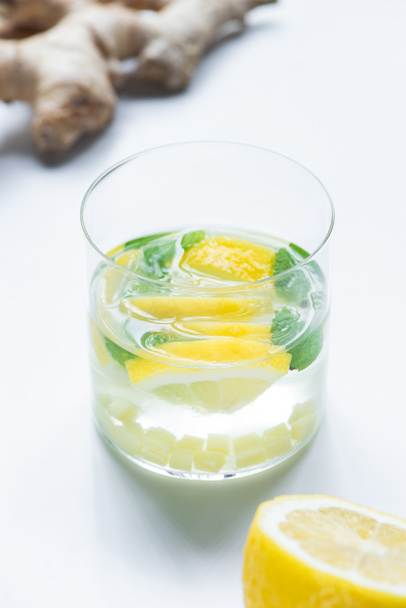 szelektív fókusz a friss limonádé üveg közelében citrom és gyömbér gyökér fehér alapon - Fotó, kép