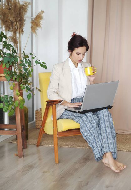 Woman with laptop works from home. Woman in office jacket and home pants communicates with workers. Remote work concept. - Photo, Image