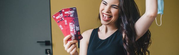 panoramic shot of excited girl holding medical mask and night party tickets, end of quarantine concept  - 写真・画像
