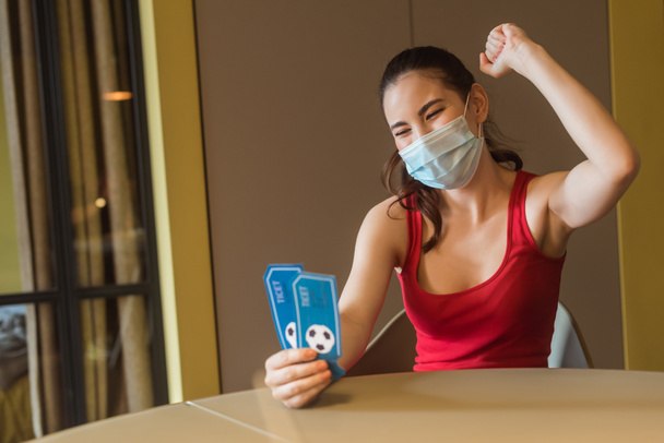 χαρούμενη γυναίκα με ιατρική μάσκα που κρατάει αθλητικά εισιτήρια αγώνων  - Φωτογραφία, εικόνα