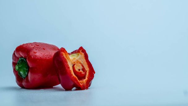Red bell pepper with chopped portion on blue gradient background in the left side of the frame - Zdjęcie, obraz