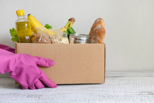 Volunteer in gloves contactless delivery food. Box with stocks, vegetables, cereals, bread, fruits - Fotoğraf, Görsel