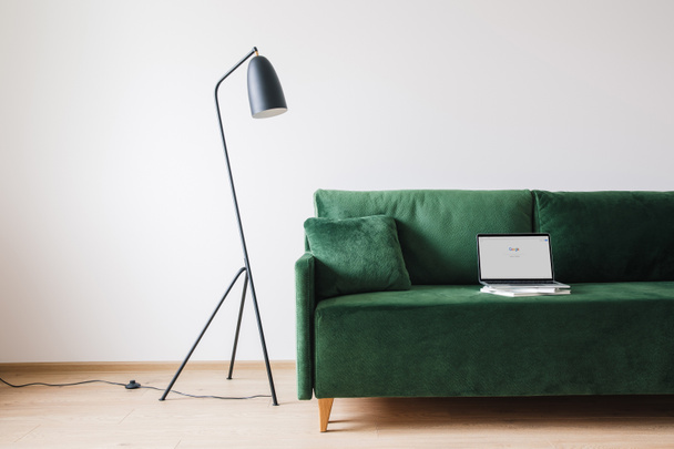 KYIV, UKRAINE - APRIL 14, 2020: green sofa with pillow and laptop with google website on screen near metal modern floor lamp - Foto, Imagen