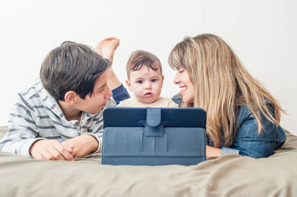 μπροστινή όψη μιας χαρούμενης οικογένειας χρησιμοποιώντας το tablet στο κρεβάτι. - Φωτογραφία, εικόνα