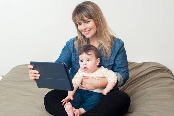 Maman utilisant la tablette im lit et tenant son nouveau-né sur ses genoux. Grand espace de copie
. - Photo, image