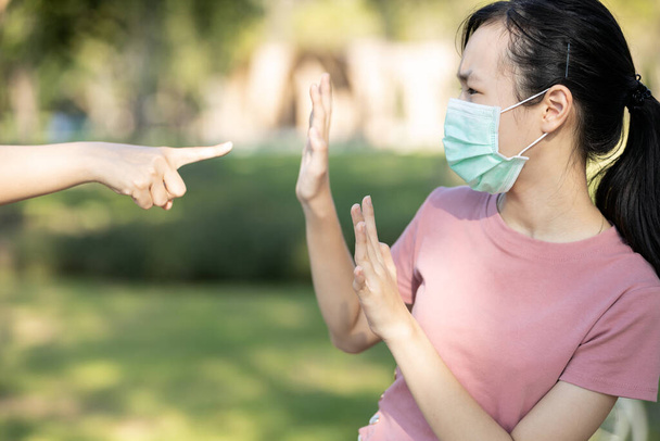 Trieste aziatische meisje student in hygiënisch masker tijdens de pandemie van Coronavirus of Covid-19, hand wijzende vinger naar bang kind meisje, pestende slachtoffer en haat, anti-racisme, stoppen xenofobie, gepest door de samenleving - Foto, afbeelding