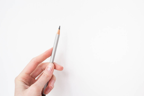 白いキャンバスの背景に手に1つの灰色の鉛筆。鉛筆で描く。隔離中の趣味。インスピレーション、才能。新しい絵、スケッチを作成します。芸術家だ。美術. - 写真・画像