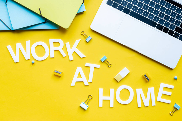 Вид сверху на работу дома, рядом ноутбук и канцелярские принадлежности на желтом фоне
 - Фото, изображение