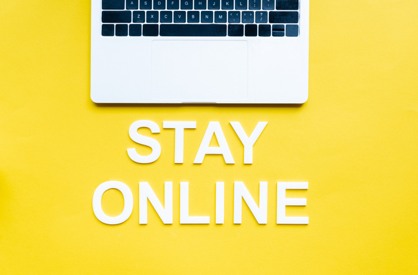 Top view of stay online lettering and laptop on yellow surface - Fotoğraf, Görsel