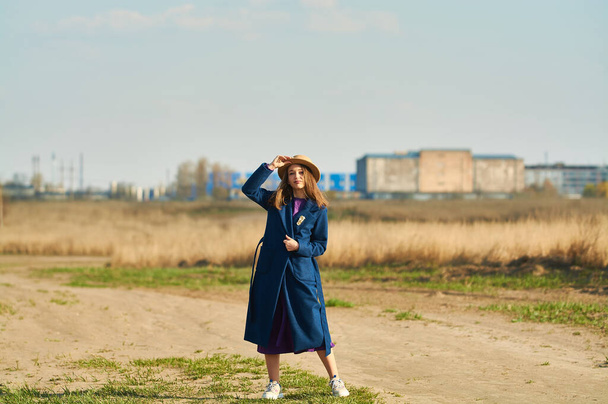 Šťastná mladá dáma v modrém kabátě s béžovým kloboukem běží na poli brzy na jaře. - Fotografie, Obrázek