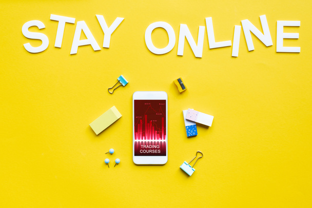 Top view okostelefon kereskedési tanfolyamok app, irodai kellékek és marad online felirat sárga felületen - Fotó, kép