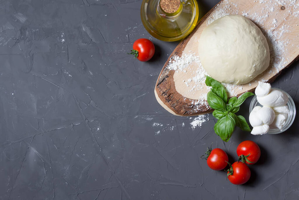 Surová pizza ingredience na šedé desce s kopírovacím prostorem, těsto, rajčata, mozzarella, bazalka, olej - Fotografie, Obrázek