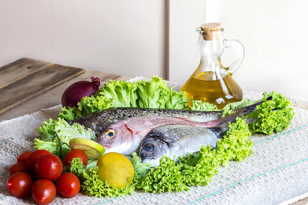 pescado mediterráneo fresco: Diplodus, pandora común o pagellus, con limón y tomates, ensalada verde y aceite de oliva en la cocina casera
 - Foto, imagen