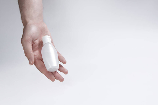 een kleine fles voor crème, vloeistof of ontsmettingsmiddel in de hand op een witte achtergrond. kopieerruimte - Foto, afbeelding