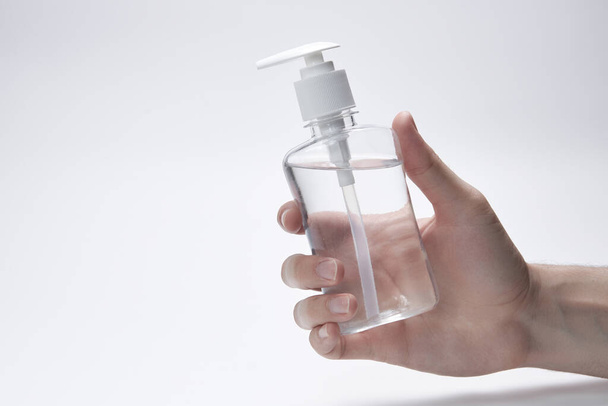 Main tient une bouteille transparente, une bouteille ou un récipient pour gel, crème ou antiseptique sur un fond blanc. copyspace
 - Photo, image