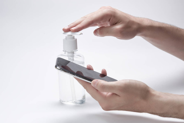 Disinfection of the phone. Hands hold smartphone and bottle or container for antiseptic cream or gel white background. - Photo, image
