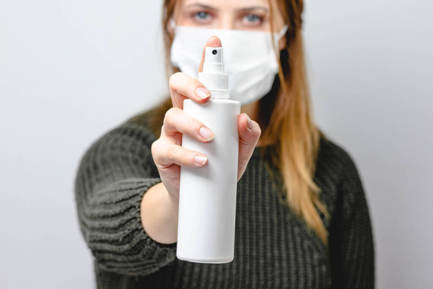 Una mujer con una máscara médica en la cara sostiene un desinfectante en sus manos. Protección contra virus e infecciones. Quédate en casa, virus corona.. - Foto, imagen