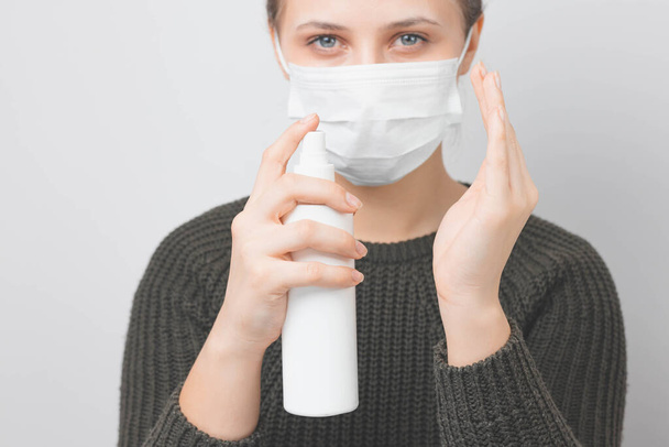 Kobieta z maską medyczną na twarzy dezynfekuje ręce w domu. Ochrona przed wirusami i zakażeniami. Zostań w domu, wirusie korony.. - Zdjęcie, obraz