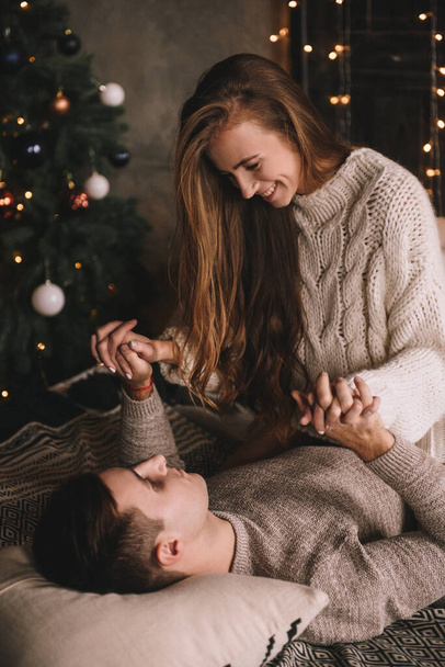 Couple on the bed in the bedroom. Dark interior. New Year's and Christmas. Hugs and kisses. Love. White sweater and high socks. Romantic meeting. A date lovers. - 写真・画像